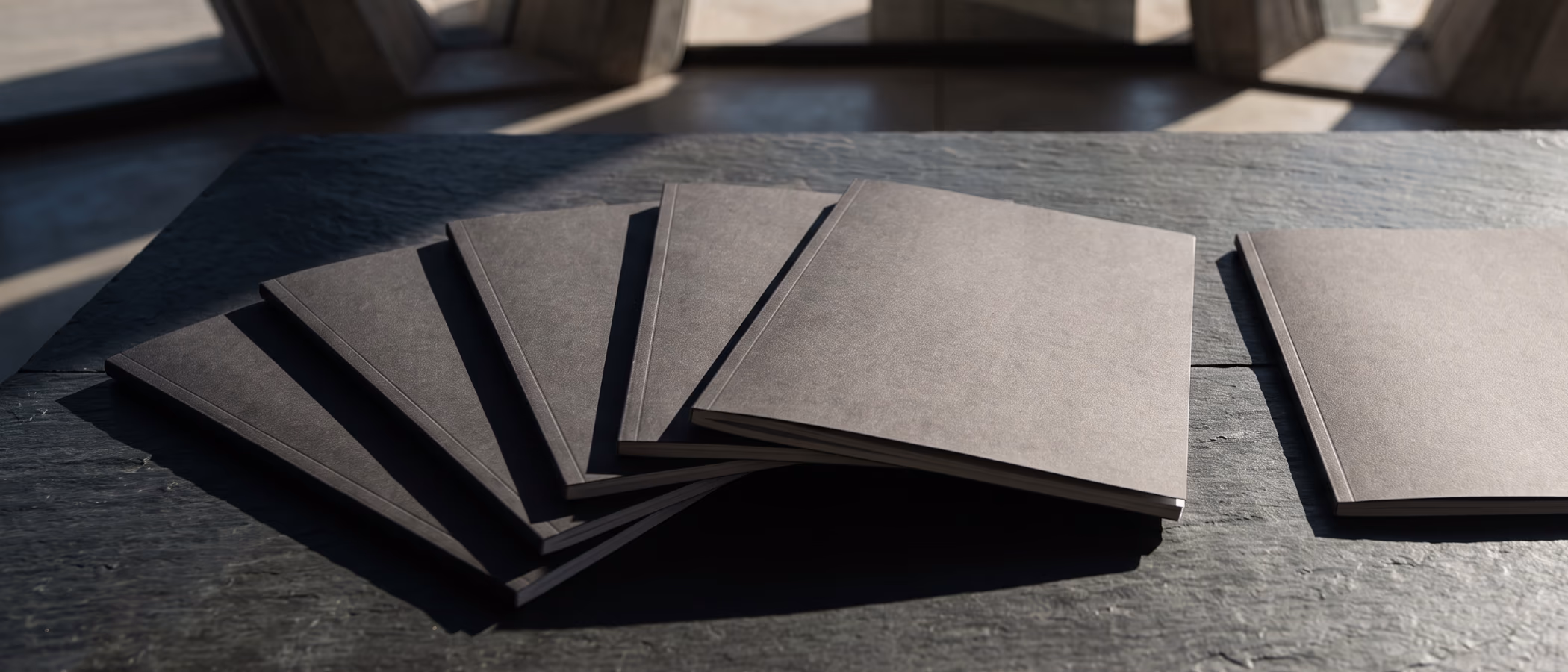 Six identical charcoal report covers fanned in a precise overlapping row on dry slate